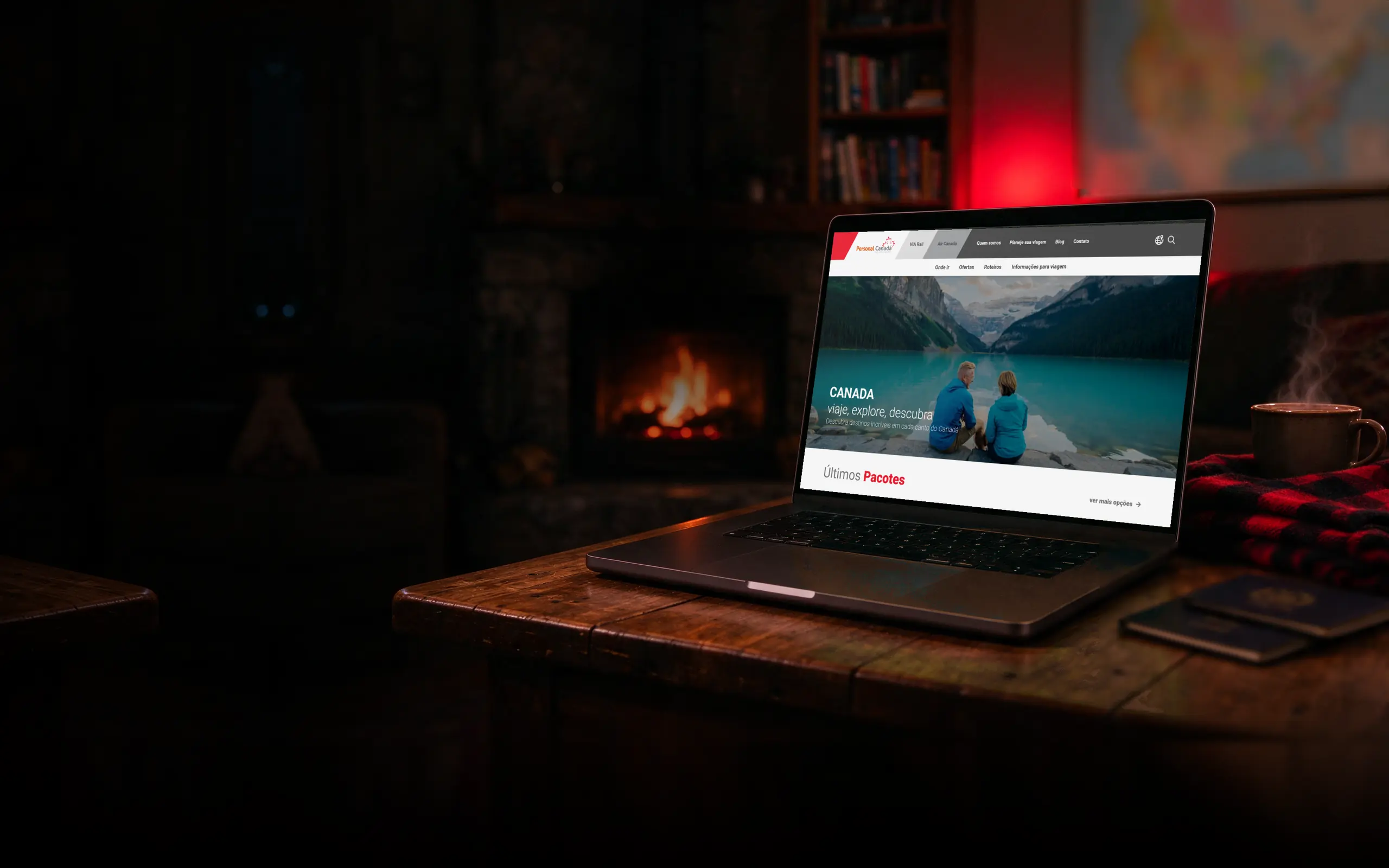 Notebook sobre a mesa de centro de madeira de uma sala de estar à noite, com lareira acesa e manta xadrez, exibindo o site da Personal Canadá